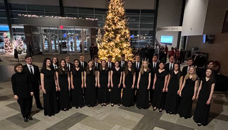 Choir in concert dress beside a Christmas tree
